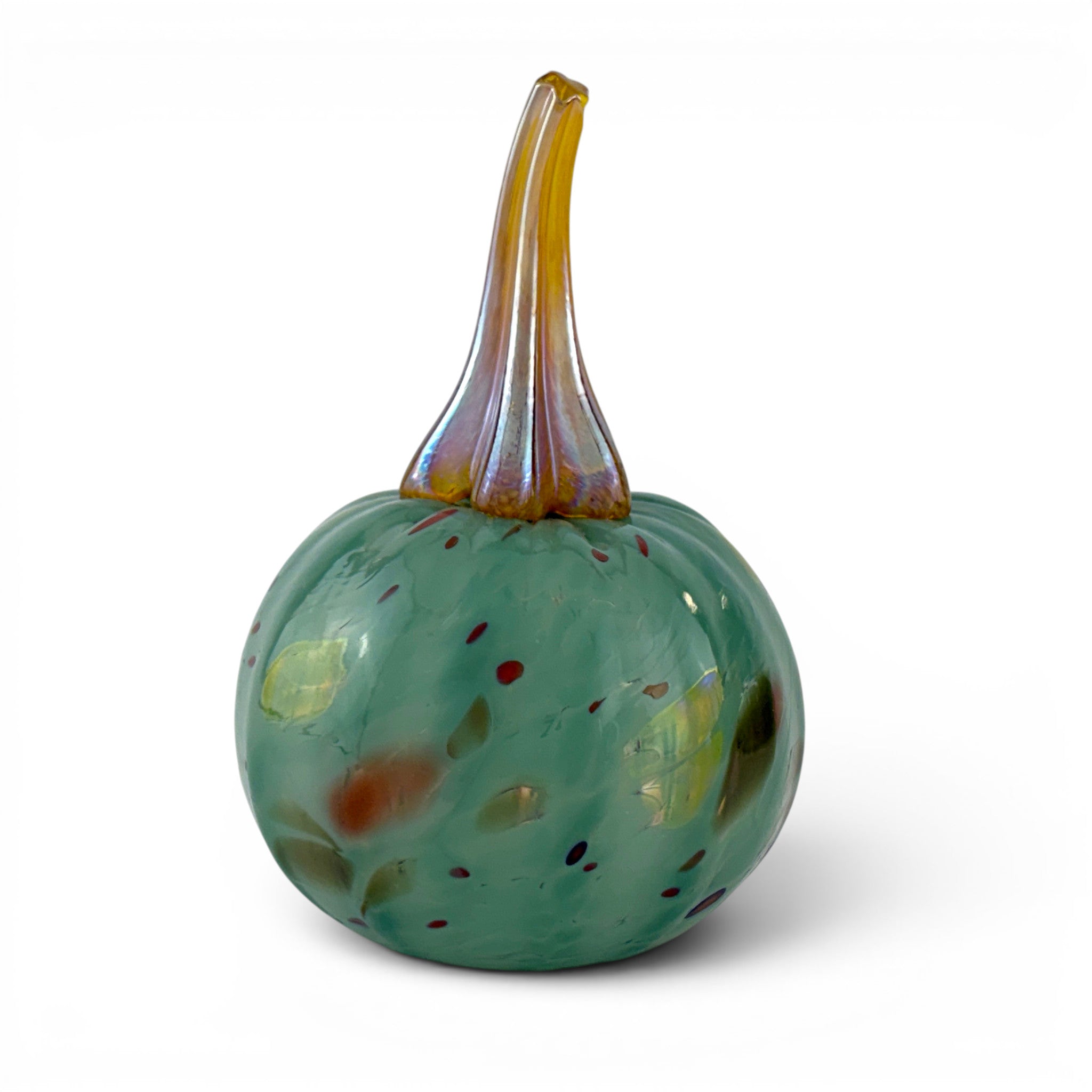 A hand-blown glass decorative pumpkin with a rounded teal-green body speckled with small amber, yellow, and red flecks, and a curved amber glass stem, shown on a white background.