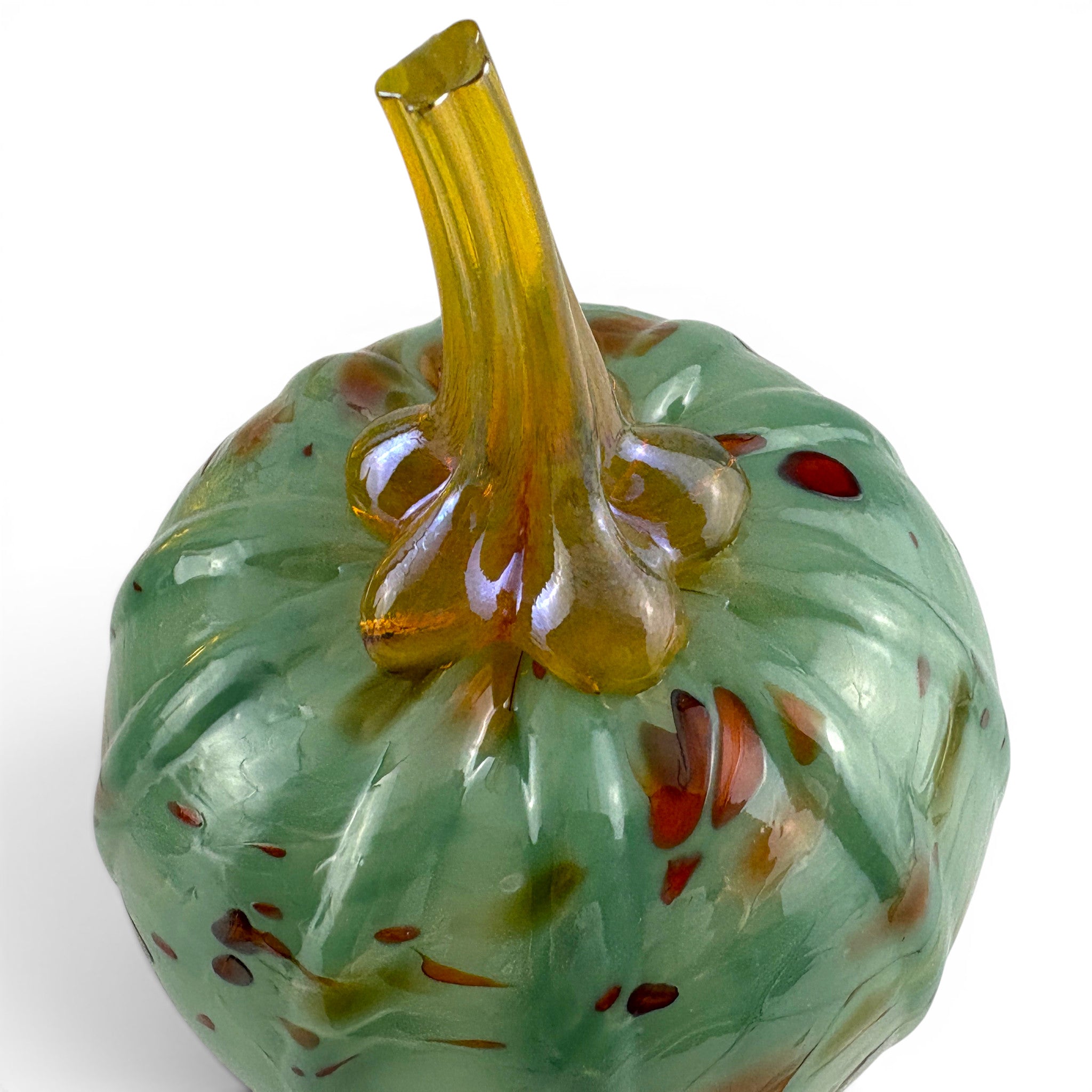 A decorative glass pumpkin with a glossy light green body, speckled with small red and orange flecks, and a thick translucent amber-yellow stem, shown on a white background.