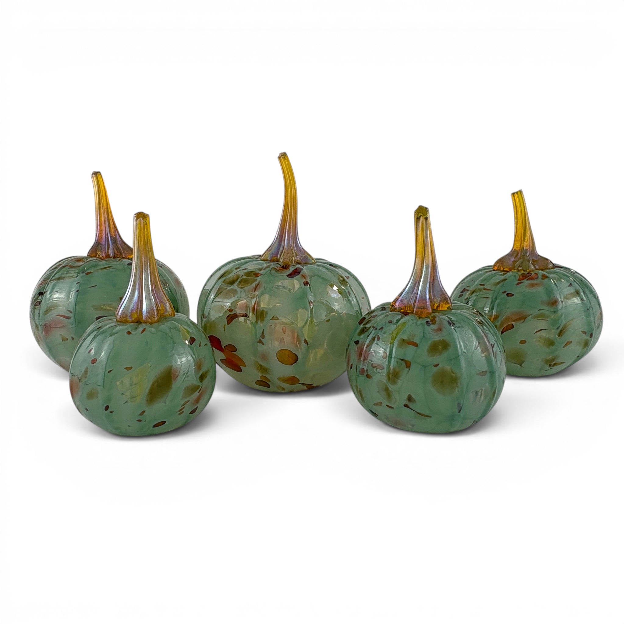 Five decorative glass pumpkins in a speckled green and amber-brown style, arranged on a plain white studio background.