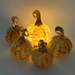 Four decorative glass pumpkins arranged together, glowing warmly from an internal light. The pumpkins are translucent amber and yellow with orange speckles and metallic gold-toned stems, set against a softly lit neutral background.