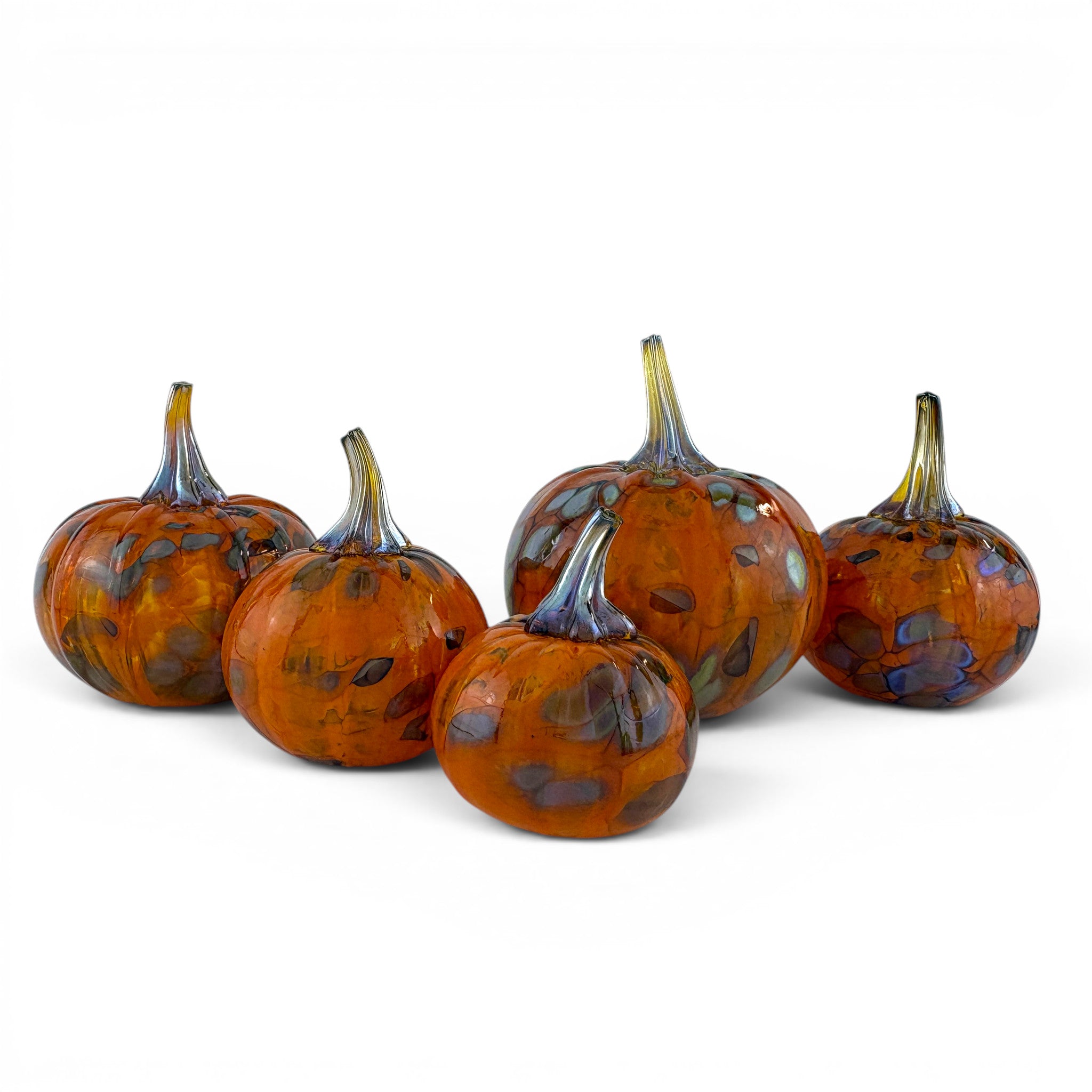 Five decorative glass pumpkins in orange and amber tones with blue-gray marbling and stems, arranged on a white studio background.
