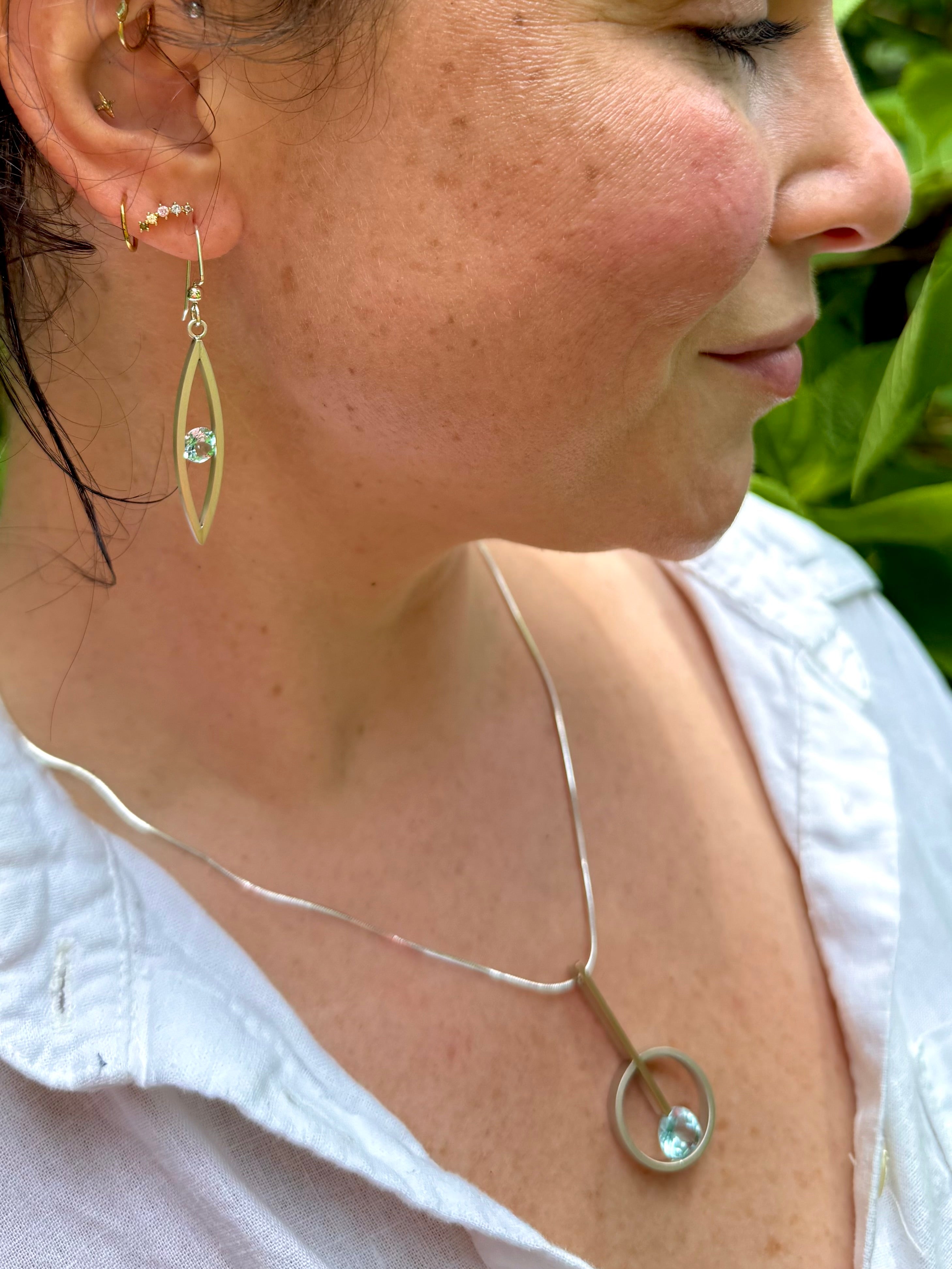 Close-up of a woman wearing gold and sterling earrings and a silver necklace with blue topaz gemstones.