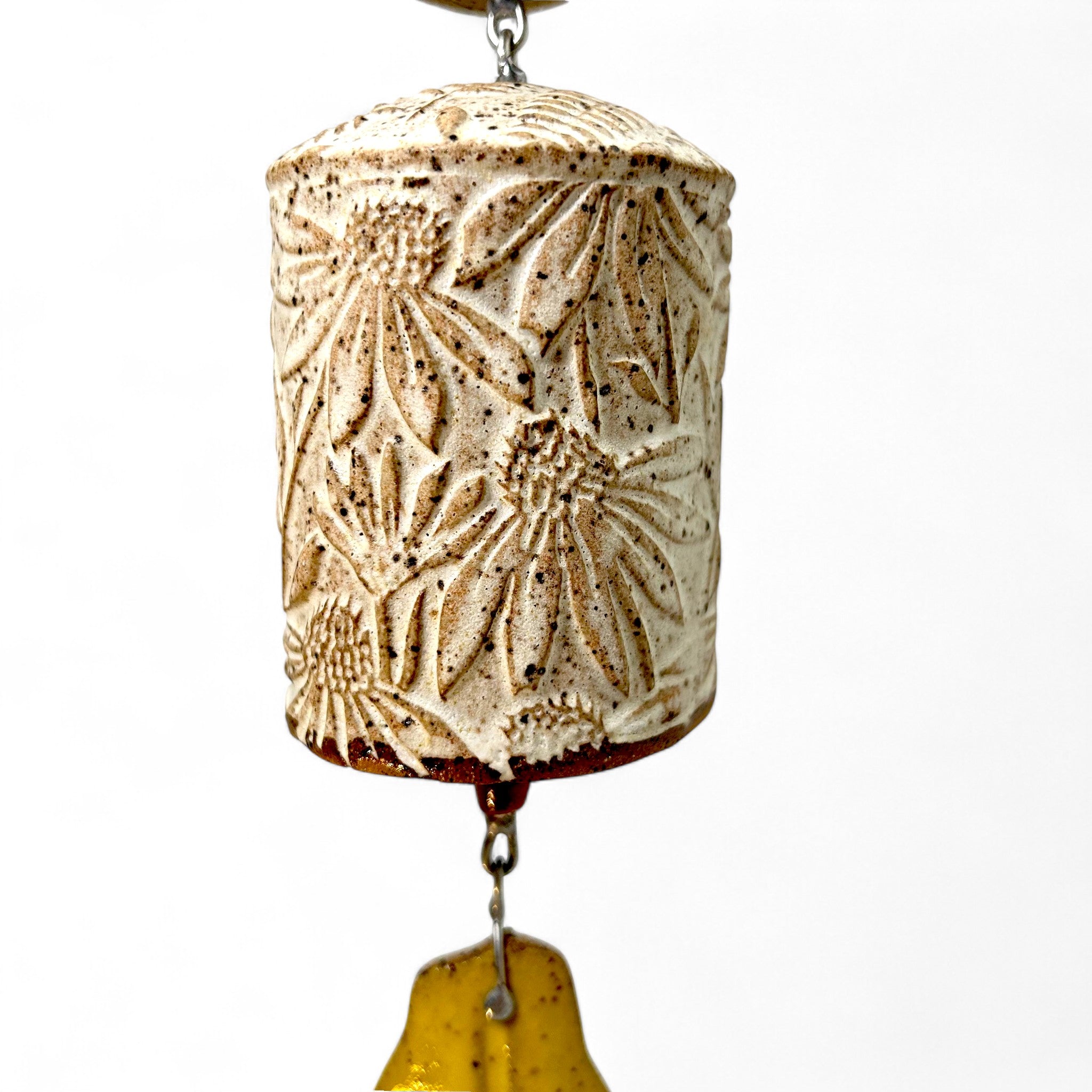 Decorative ceramic bell with floral cone flower patterns attached to a handcrafted chain and leaf