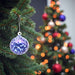 Decorative blue ornament on a Christmas tree with a blurred background of colorful lights.