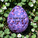 Decorative egg with purple and pink speckles on grass with flowers