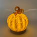 A glowing hand-crafted glass pumpkin  with a textured ribbed body and warm amber stem, displayed on an LED light with a wooden base.  