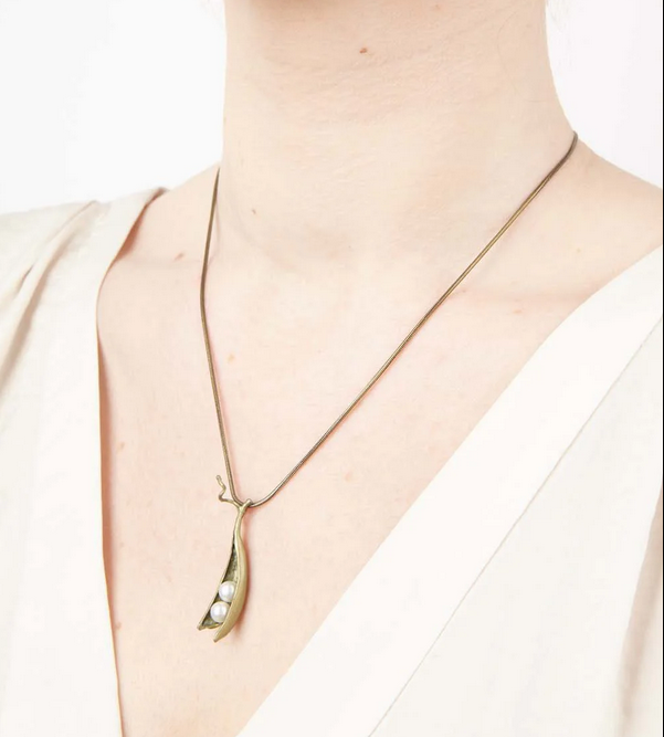 A cast bronze pea pod necklace with two earls on a model
