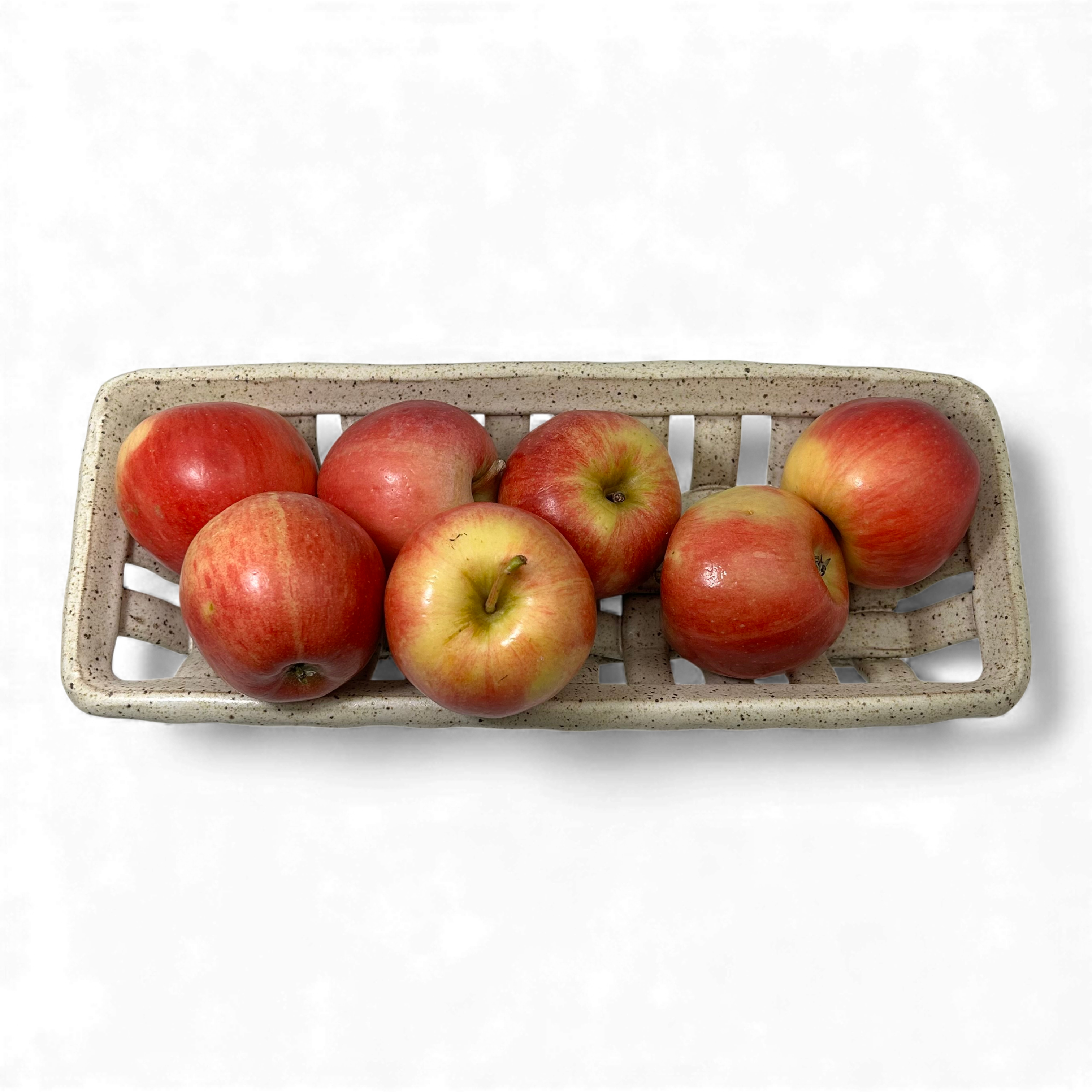 Apples in a hand-crafted rectangular ceramic basket on a white background