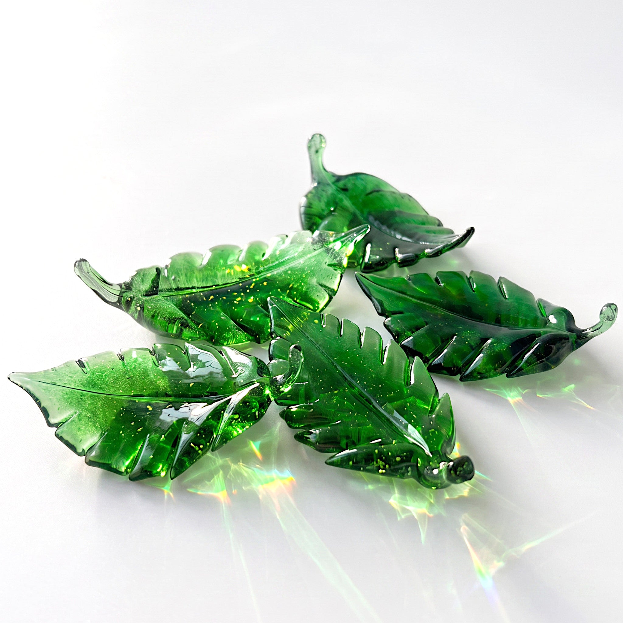 Five green translucent glass leaf sculptures with light reflections.