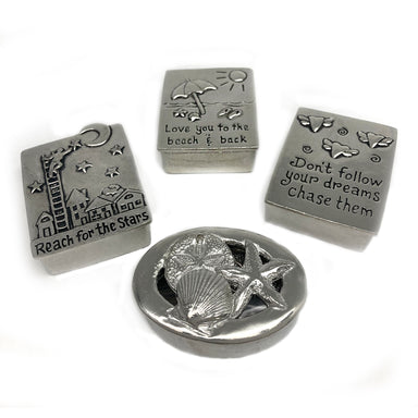 Four pewter wish boxes with different designs including seashells, stars, a lighthouse, and text phrases, each with a matching necklace on a chain.