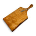 A free-form wooden serving board with a live edge and a rounded handle, shown with a small pewter pate utensil resting on top.
