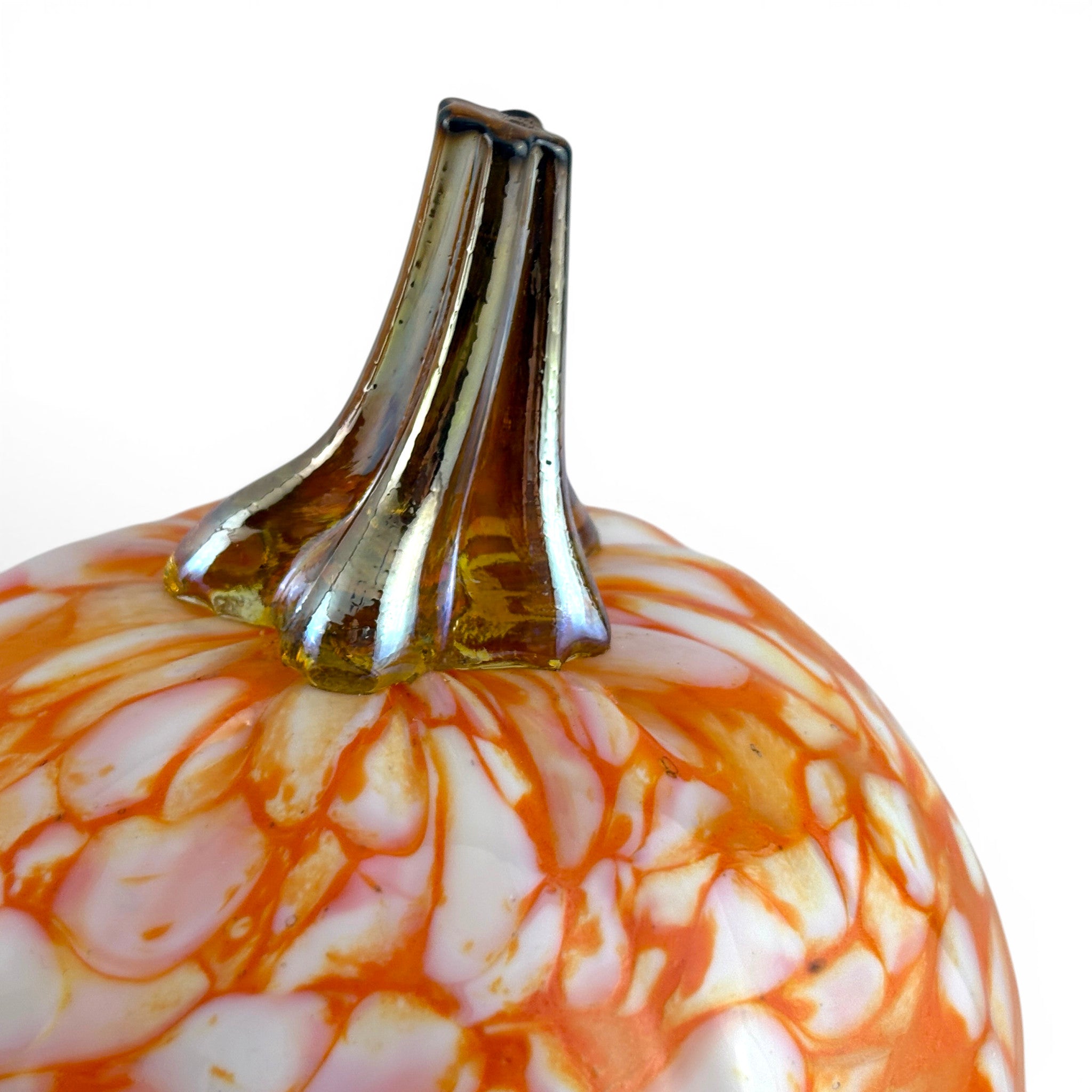 A close-up of a decorative glass pumpkin with a glossy orange and white marbled pattern and a flared metallic gold stem, set against a plain white background.
