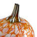 A close-up of a decorative glass pumpkin with a glossy orange and white marbled pattern and a flared metallic gold stem, set against a plain white background.