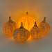 Five decorative glass pumpkins arranged together, glowing warmly from an internal light. The pumpkins have a textured, marbled pattern in orange and cream, with short brown stems, set against a plain light background.