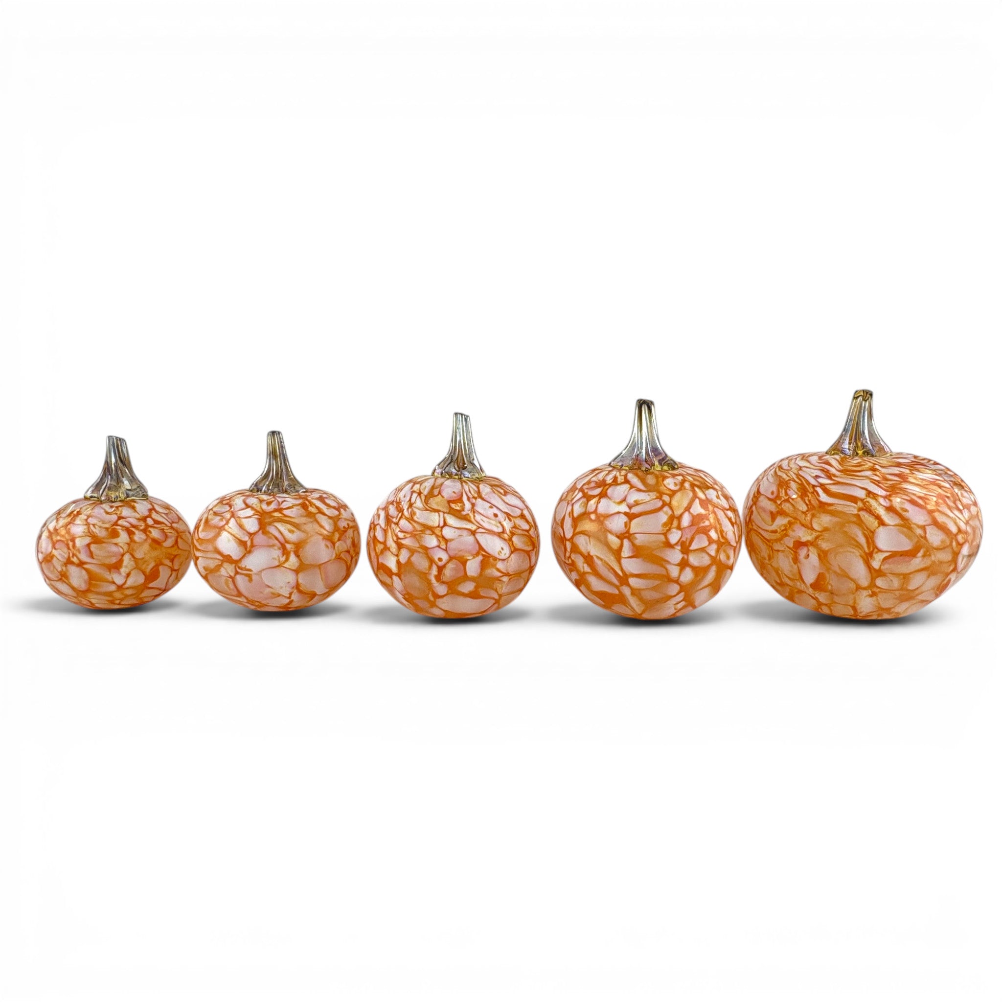 Five decorative glass pumpkins arranged in a row, varying in size, featuring an orange and white marbled pattern with metallic silver stems, set against a plain white background.