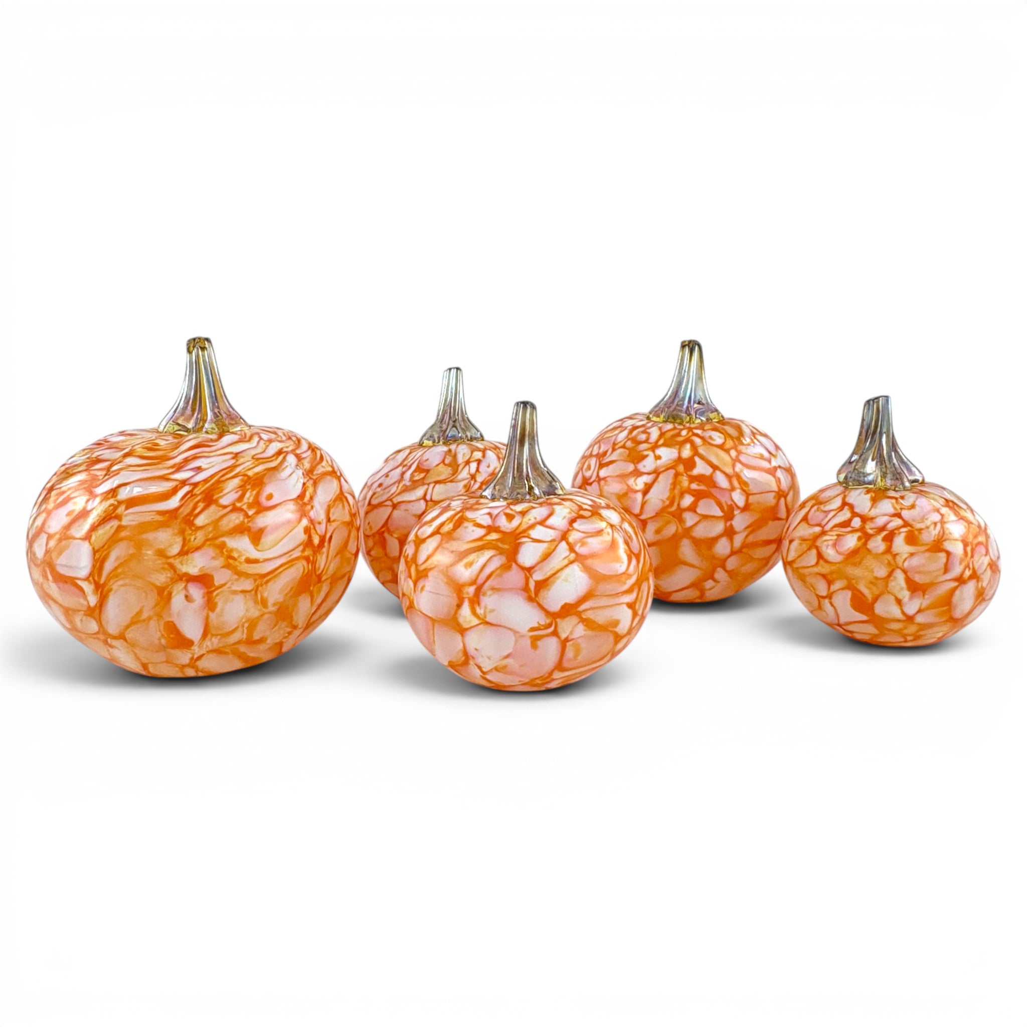 Five decorative glass pumpkins in graduating sizes, featuring an orange and white marbled pattern with metallic silver stems, arranged on a white background.