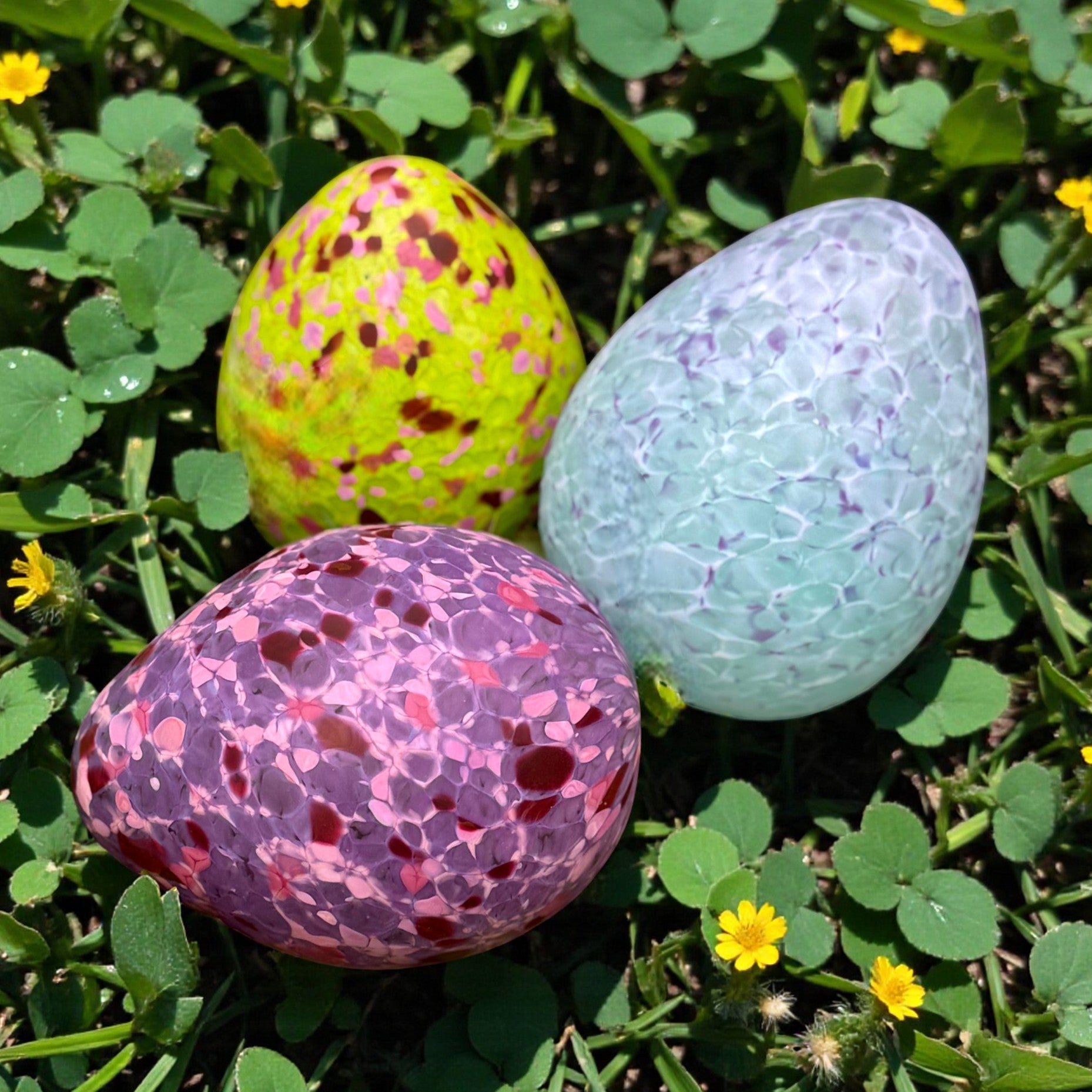 Colorful handblown glass eggs on grass with yellow flowers