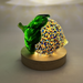 A decorative glass acorn displayed on a round wooden base LED light display against a softly lit neutral background.