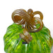 A close-up of a hand-blown glass pumpkin with a ribbed green body and a thick, glossy amber-brown stem.   