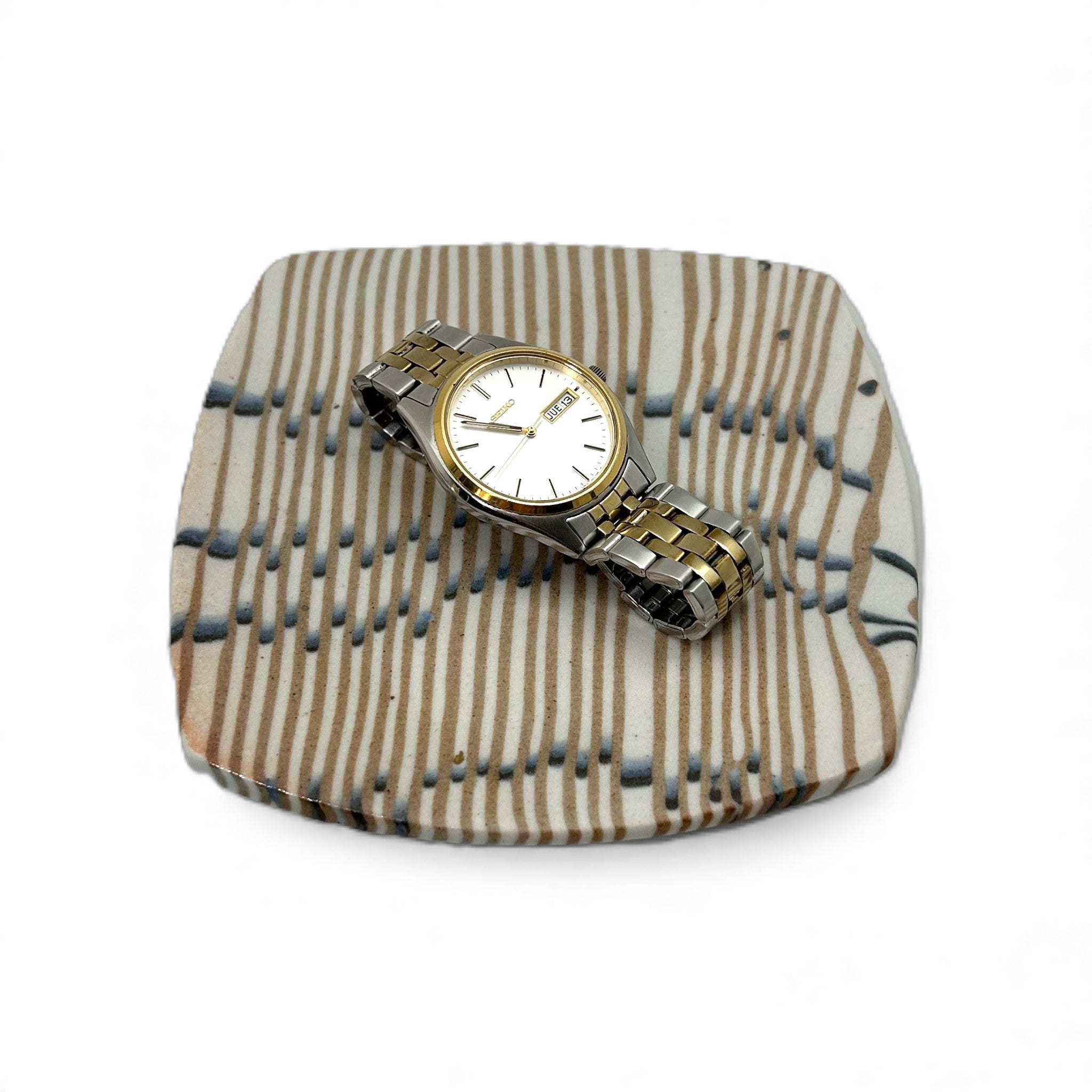 Wristwatch on a small, textured square, colored porcelain plate