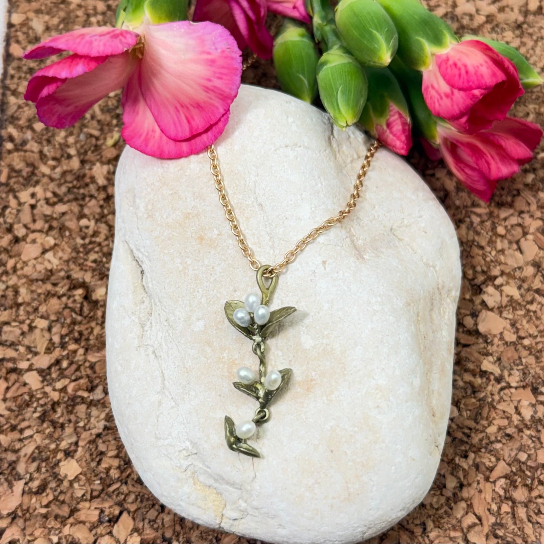 Necklace with a leaf and pearl design on a white stone with pink flowers in the background