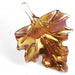 A glass sculpture of an amber leaf with a metallic sheen, designed for hanging or flat display.