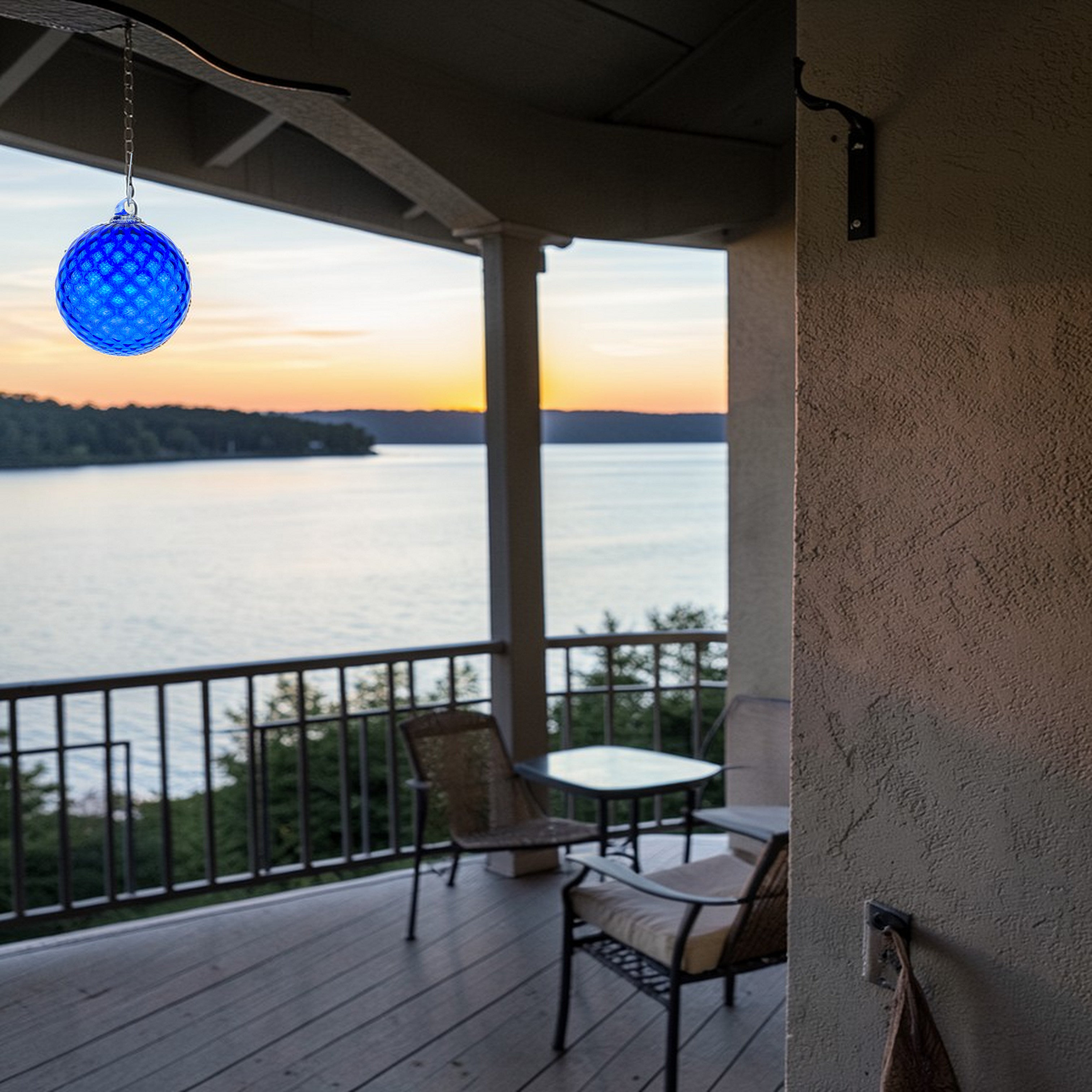 Outdoor deck with a view of a lake at sunset, featuring a blue hanging, textured glass infinity globe.