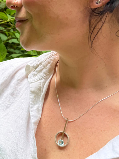 Close-up of a person wearing a silver and gold fill necklace with a blue topaz necklace.