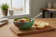 Bowl of salad with a side of bread on a wooden cutting board in a bright room.