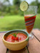 Bowl of gazpacho with a colorful glass of tomato soup on a wooden surface outdoors.
