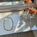 Colorful beaded necklace on a glass surface with a vase of flowers and a bottle of perfume.