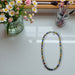 Colorful beaded necklace on a white surface with flowers and makeup brushes in the background
