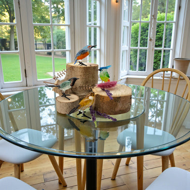 Decorative bird figurines on a glass table with a view of a garden.