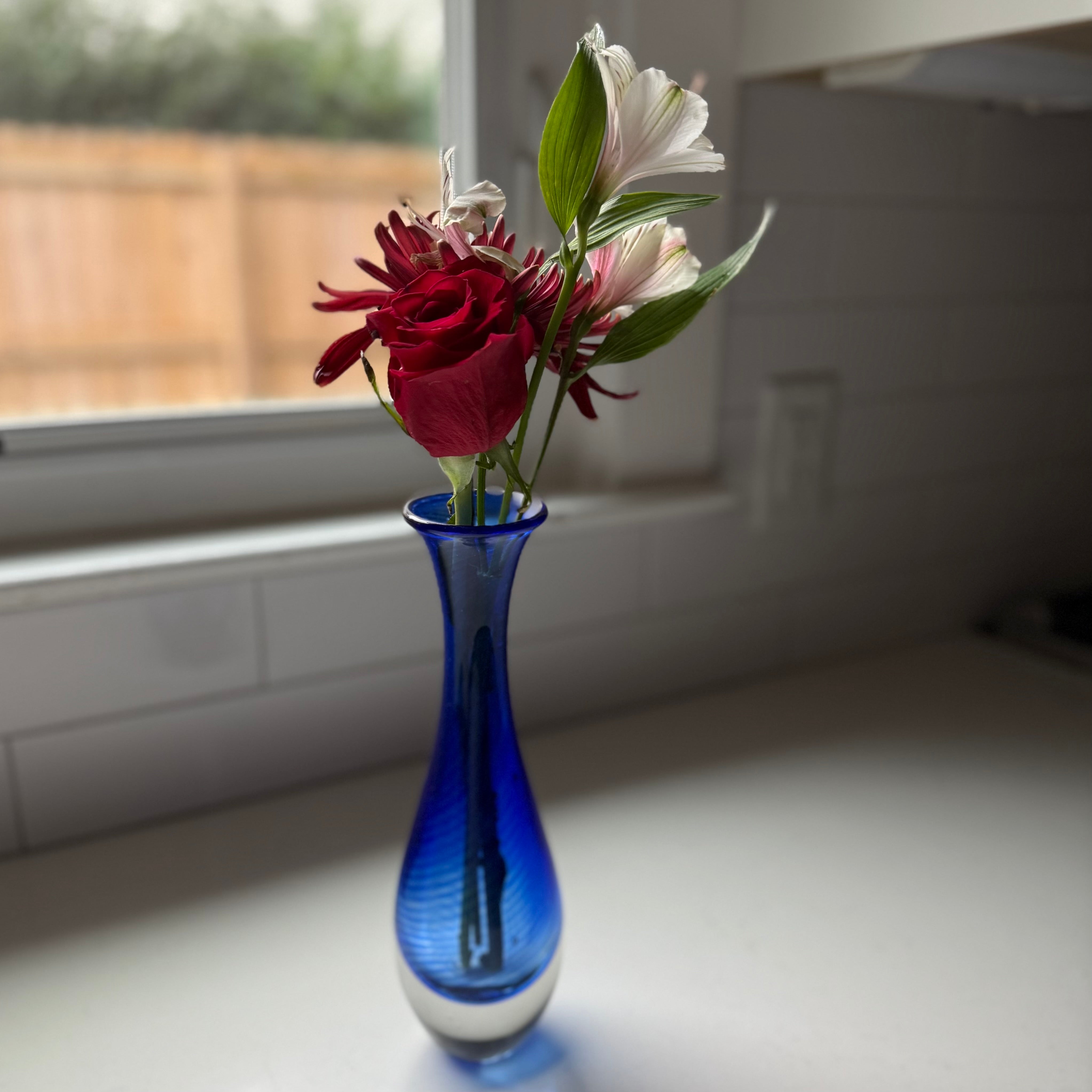 Blue vase with red and white flowers on a windowsill