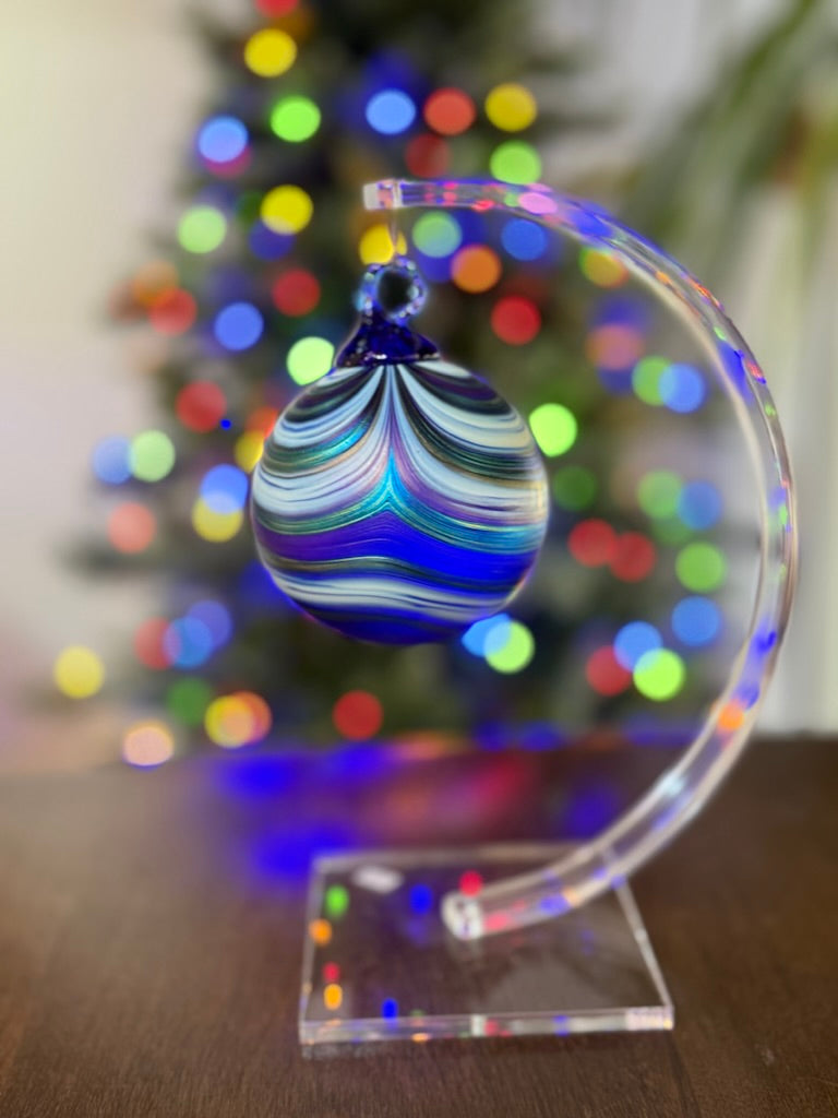 Decorative glass ornament on a stand with a Christmas tree in the background
