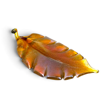 A handcrafted translucent amber glass leaf sculpture with a small gold-toned stem at the top.  