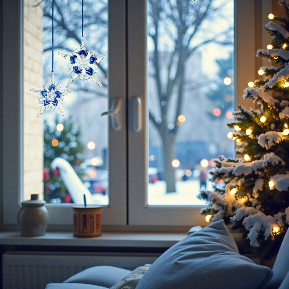 Decorative snowflake ornaments hanging by a window with a Christmas tree in the background.