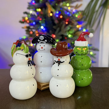 four handcrafted glass snowmen grouped with a holiday tree