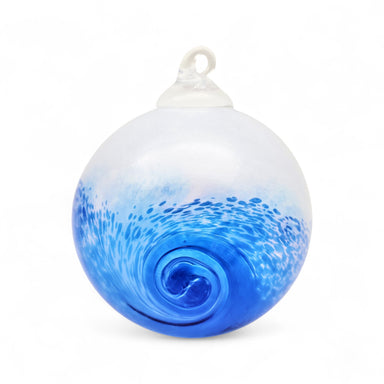 A hand blown glass ornament with a wave design, predominantly blue, with a white top presumably for hanging.