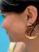 Close-up of a person wearing gold hoop earrings with a clear blue sky background