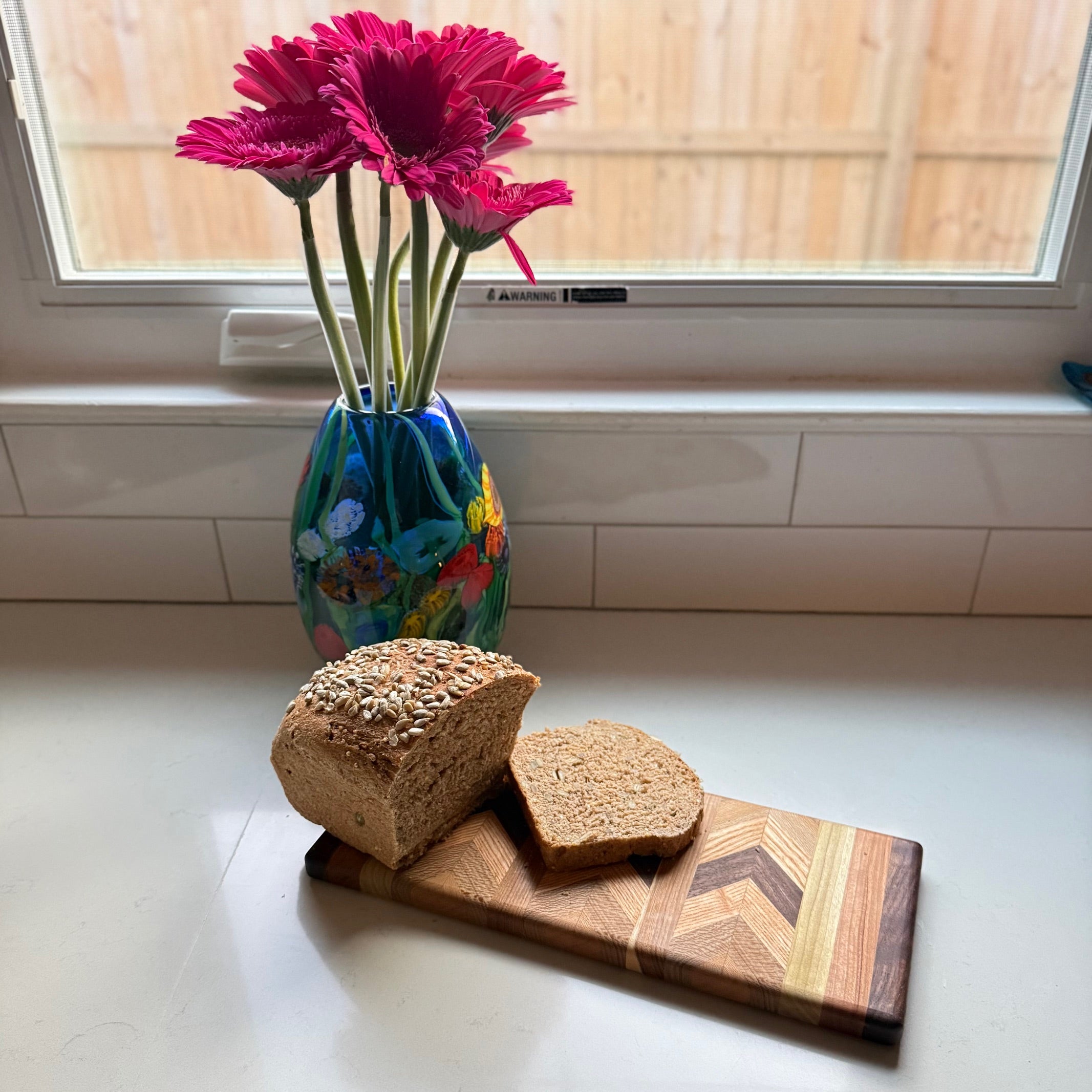 Loaves of bread on a handcrafted wooden cutting board with a vase of pink flowers in the background.