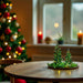 Decorative Christmas trees on a table with a blurred Christmas tree in the background.