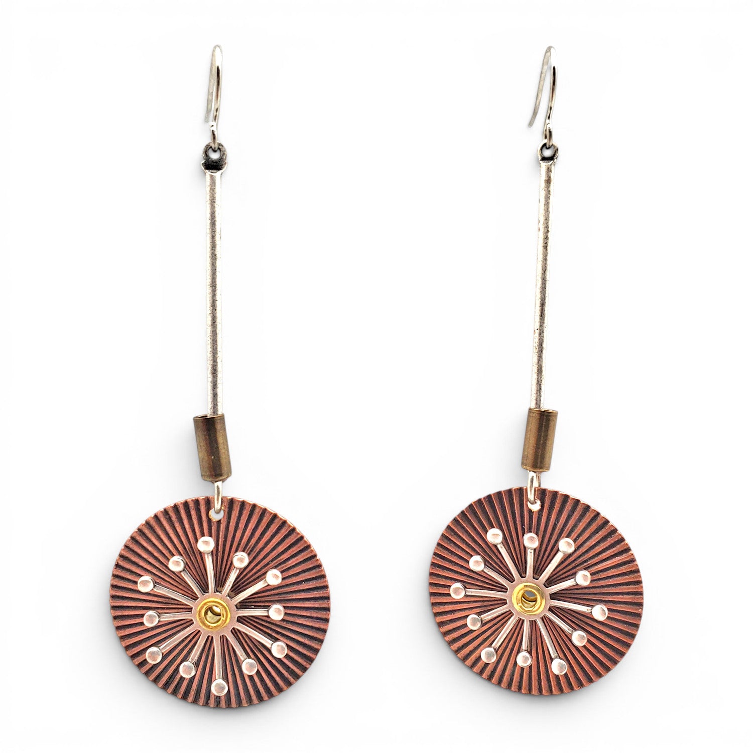 A pair of dangling earrings with circular sunburst-patterned wooden discs in reddish-brown and black, accented with small white dots and a gold center, hanging from silver-toned wires on a white background.