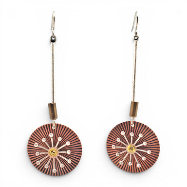 A pair of dangling earrings with circular sunburst-patterned wooden discs in reddish-brown and black, accented with small white dots and a gold center, hanging from silver-toned wires on a white background.