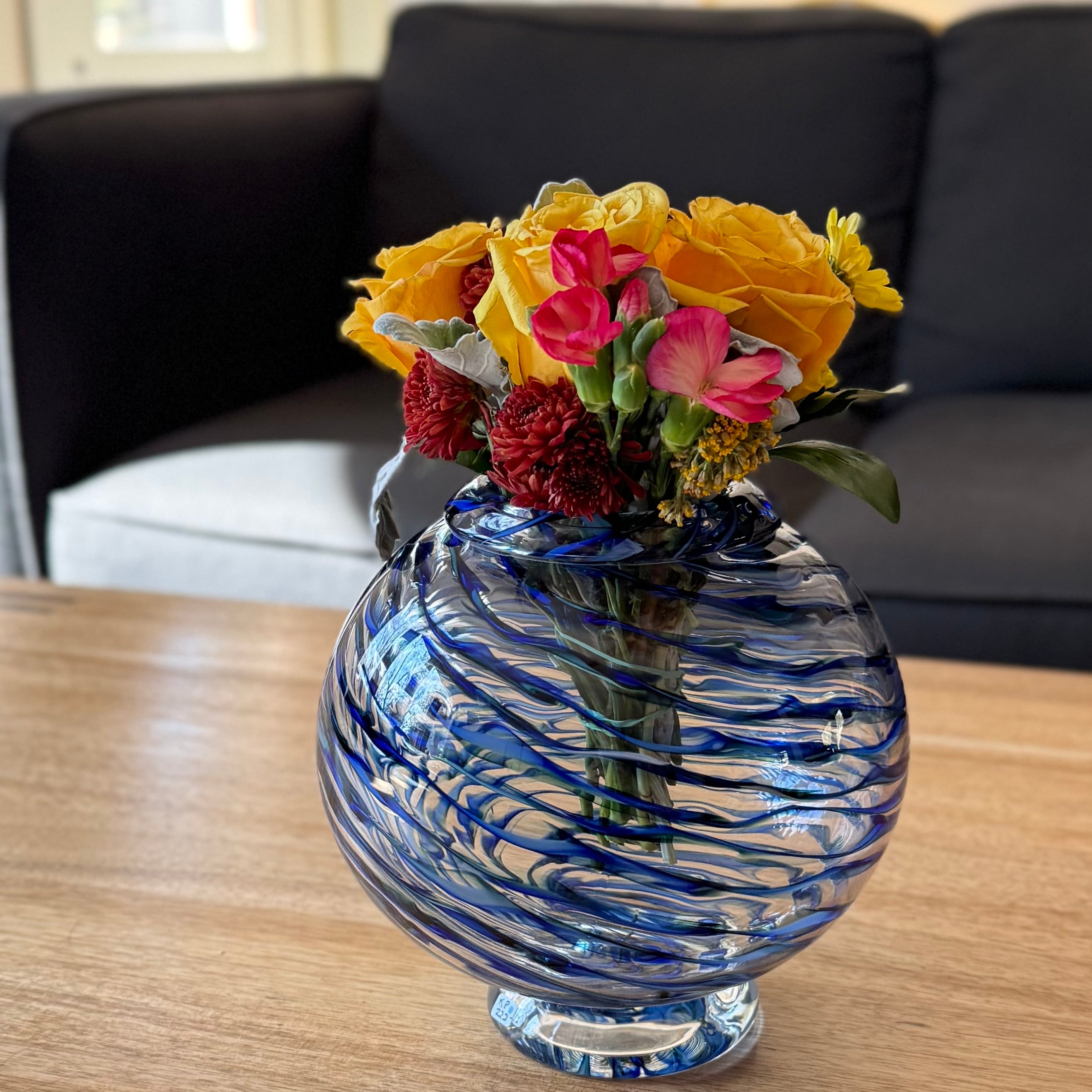 Handcrafted blue glass vase with colorful flowers on a wooden table livens up your home with color and design