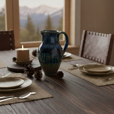 Dining table setting with a pitcher, plates, and candles in a room with mountain views.