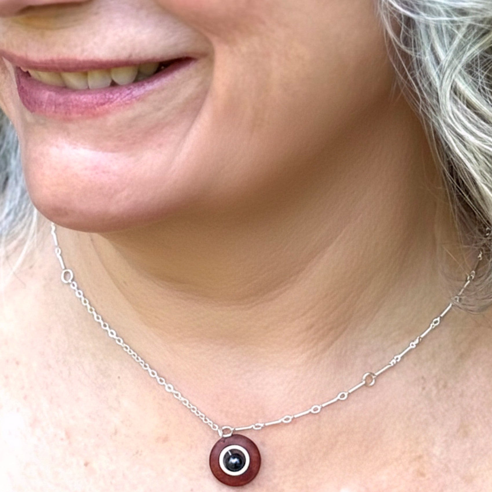 Close-up of a person wearing a silver necklace with a red pendant.