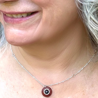 Close-up of a person wearing a silver necklace with a red pendant.