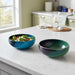 Two colorful handcrafted ceramic bowls on a kitchen counter, one with salad.