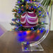 Decorative Christmas ornament on a clear stand with a Christmas tree in the background.
